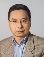 Steven is smiling and wearing a brown, checkered blazer.